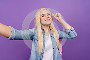Self-portrait of attractive cheerful brainy girl touching specs going back to school isolated over bright violet purple