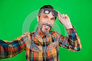 Self-portrait of attractive cheerful man touching specs posing good mood isolated over bright green color background