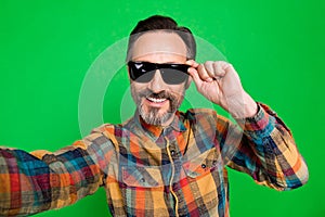 Self-portrait of attractive cheerful man touching specs summertime  over bright green color background