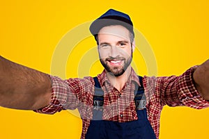 Self portrait of joyful cheerful mechanic with stubble in blue overall, shirt shooting selfie on front camera with two