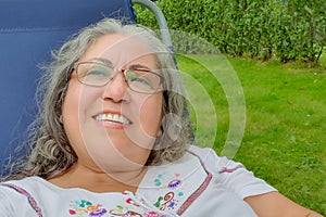 Self portrait of smiling face of a beautiful chubby Mexican woman, sitting on a sunbathing chair