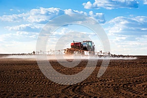 Big red self-propelled red sprayer with long arms disperses fertilizers on agricultural fields, rear view with beautiful clouds