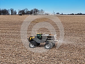 Self propelled spreader applying fertilizer to a field before tilling with farm scene in the distance