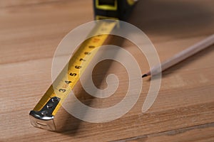 Self retracting metal measuring tape and pencil on wooden table, closeup