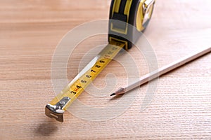 Self retracting metal measuring tape and pencil on wooden table, closeup