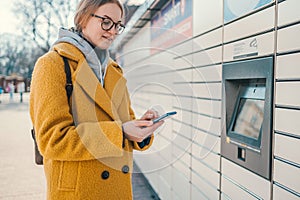 Self service post terminal machine and parcel sending. Woman holding smartphone using red automated self service post