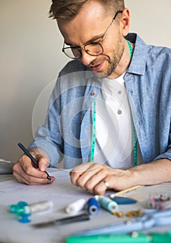 A self-taught seamster with glasses is working at the table. A DIY designer draws a sketch for a new costume project. A smiling