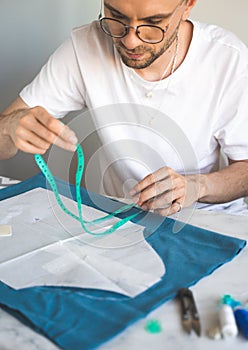 A self-taught seamster in white t-shirt and glasses works with fabric, pattern and chalk. A tailor uses a measuring tape during