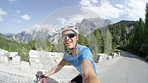 SELFIE: Athletic man laughs while he pedals uphill in the picturesque mountains.