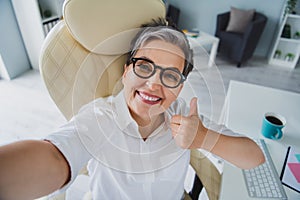 Selfie cadre of showing her workplace funny pensioner businesswoman thumb up showing respect employer isolated on office