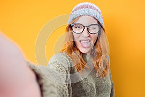 Selfie. Close-up funny mocked woman takes photo of himself with her smartphone while tongue sticking out, isolated on yellow