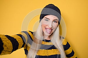 Selfie. Close-up funny mocked woman takes photo of himself with her smartphone while tongue sticking out, model wearing woolen cap photo