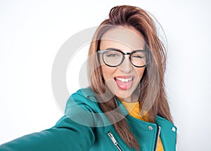 Selfie. Close-up funny mocked woman takes photo of himself with her smartphone while tongue sticking out, wearing green leather