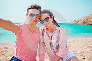 Selfie couple taking pictures on the beach in Cyclades. Tourists people taking travel photos with smartphone on summer