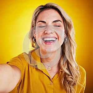 Selfie, face and smile with a laughing woman on a yellow background in studio for fun or humor. Eye closed, comic and