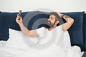 Selfie first thing in the morning. Bearded man take selfie in bed. Happy hipster smile to camera phone. Video selfie