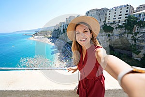 Selfie girl in Tropea, Italy. Young tourist woman taking self portrait with Tropea village on Coast of the Gods, Calabria, Italy