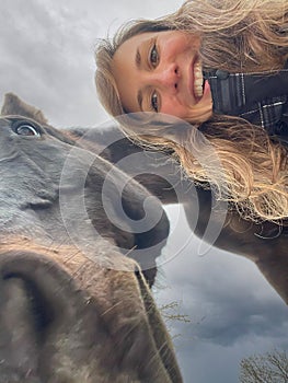 SELFIE: Gorgeous woman with curly hair poses next to her funny dark brown horse.