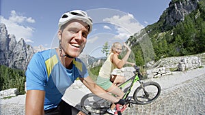 SELFIE: Happy couple on bicycle ride smiles as fit young woman waves to camera.