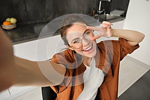 Selfie of happy young and carefree woman, taking photo on mobile phone with extended hand, posing and smiling, sitting