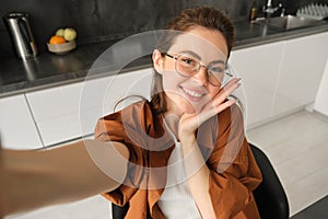 Selfie of happy young and carefree woman, taking photo on mobile phone with extended hand, posing and smiling, sitting