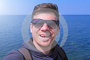 Selfie man blogger talks with subscribers on sea beach, waves hand and smiles.