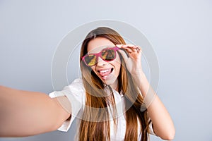 Selfie mania! Funky mood. Attractive young lady is making a selfie on the camera, flirty and playful. In pink trendy sunglasses, w