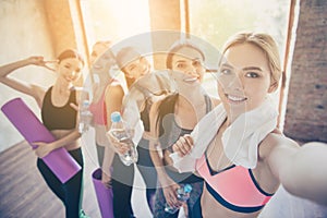 Selfie mania in gym! Five girlfriends in fashionable sport outfits are posing for a selfie photo, that blond is taking. They are