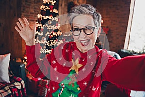 Selfie of mature aged white haired pensioner woman wear red ugly jumper new year holly jolly holiday waving palm in