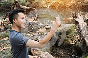 Selfie photo concept : Asian young man holding smartphone for selfies at  forest, beautiful scenery for peachful in spring , It photo