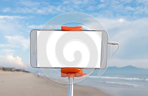 Selfie photo concept : Mock up Extensible selfie stick or monopod with mobile phone taking picture shot at sea beach and blue sky