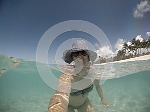 Selfie of a smiling middle aged woman in hat and shades in sea a photo