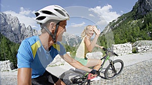 SELFIE: Sporty young woman waves joyfully to camera while the fit couple cycles.