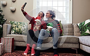 Selfie time. a cheerful young couple holding their pet dogs while taking a selfie and being seated on a sofa during