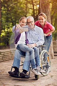 selfie time- granddaughter, daughter and disabled man in wheelchair .