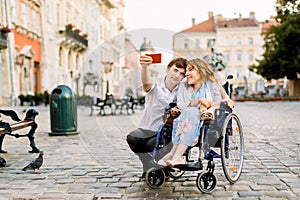 Selfie time. Handsome happy young man hugging his disabled young pretty woman and smiling while taking selfie with her