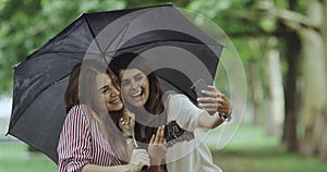 Selfie time for two ladies on rain day taking pictures using a phone , under the umbrella.4k