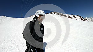 A selfie wide angle male skier aged in black equipment and white helmet rides on a snowy slope on a sunny day. The