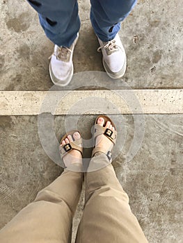 Selfie of woman and man feet in sandals on concrete floor