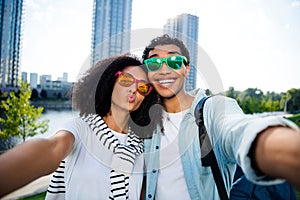 Selfie of young happy girlfriend with boyfriend pouty lips kiss and toothy smile traveling around world outdoors at