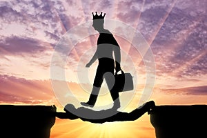 Selfish man with a crown on his head is walking over a man in the form of a bridge over an abyss photo