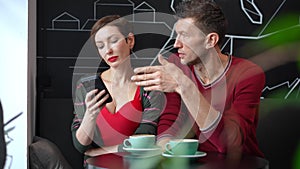 Selfish woman surfing Internet on smartphone ignoring man sitting in cafe. Sad Caucasian adult boyfriend sighing looking