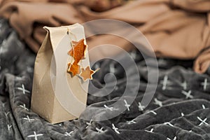 Selfmade gift box out of old beverage carton decorated with star shaped cut out dried roange peel standing on rumpled blankets on