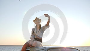 Selfphoto of Young woman to Retro car on Backlight of sunset, girl On roof of vintage automobile near sea