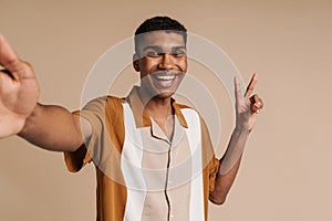 Selfportrait of young handsome smiling african man doing victory gesture