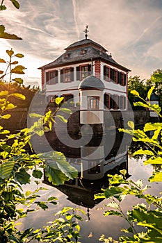 Seligenstadt moated castle in nature with a lake. with bushes and trees, reflection of the castle in the blue water