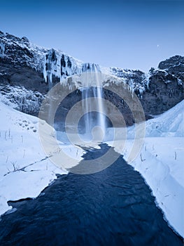 Seljalandsfoss waterfall, Iceland. Icelandic winter landscape. High waterfall and rocks. Snow and ice. Powerful stream of water f