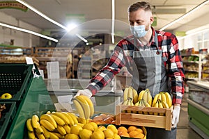 Seller in apron and mask holding bananas at market, male salesman staking fruit bananas in supermarket