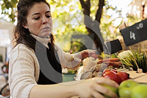 Seller arranging fresh organic produce at farmers market stand