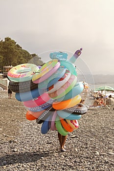 A seller with a bunch of different rubber rings strolls along the beach